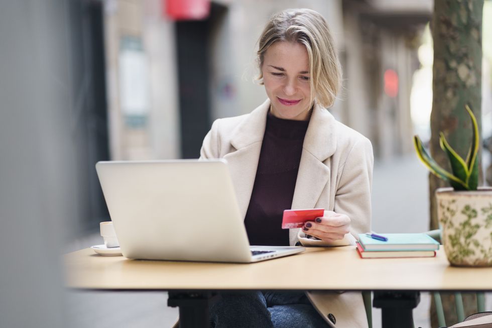 Woman sitting at a table looking at a credit card and laptop.